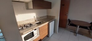 A compact kitchen with a gas stove, sink, microwave, and dishwasher. There's a small dining table with a chair. - Thermas Boulevard (Caldas Novas)