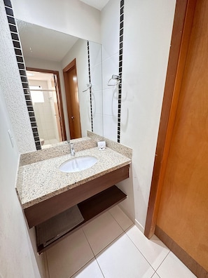 A bathroom with a granite countertop sink, a mirror, and a shower area. - Thermas Boulevard (Caldas Novas)