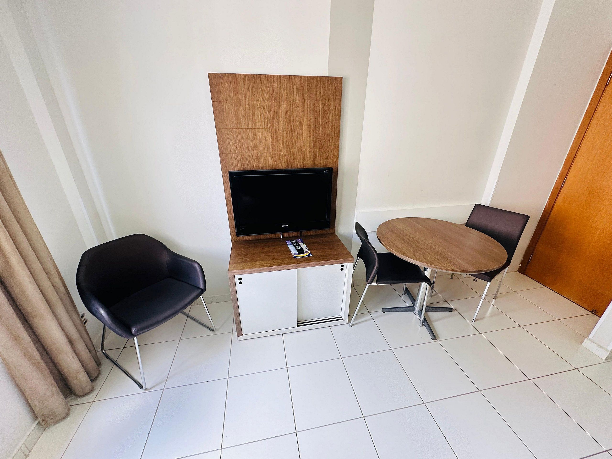 A small room with a wooden desk, a TV, two black chairs, and a round table.