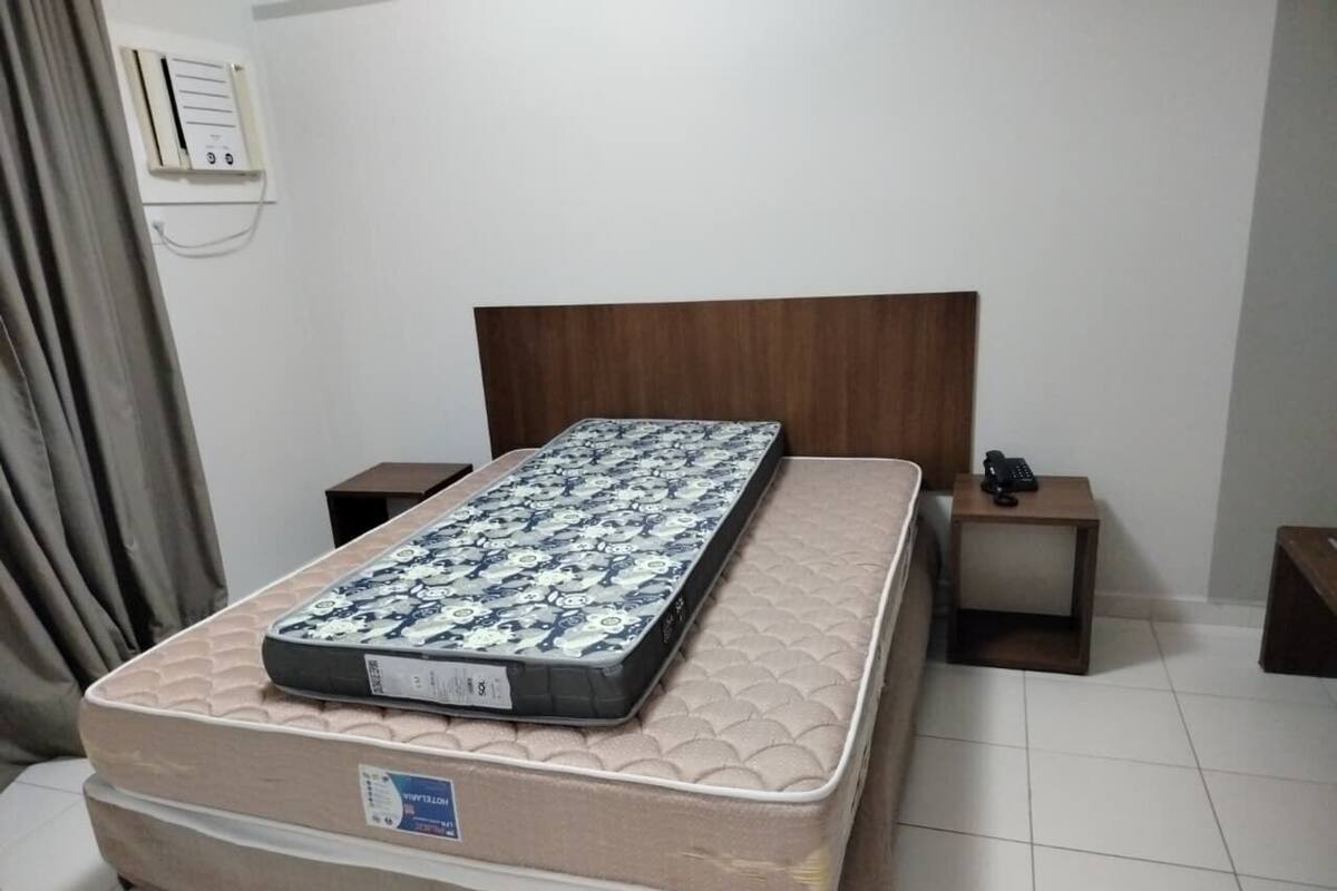 A bedroom with a large bed, a wooden headboard, two bedside tables, and a wall-mounted air conditioning unit.