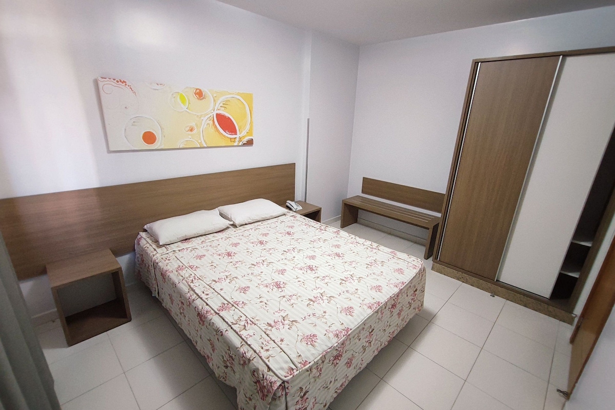A hotel room with a bed, bedside tables, a bench, a wardrobe, and a wall art piece.