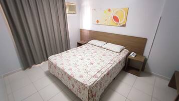 Una habitación de hotel con cama, mesita de noche, teléfono, calentador en la pared y ventana con cortinas.