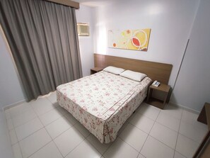 A hotel room with a bed, a nightstand, a telephone, a wall-mounted heater, and a window with curtains. - Thermas Boulevard (Caldas Novas)