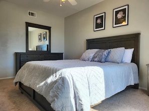 Une chambre à coucher comprenant un lit, une commode, un miroir et deux tableaux encadrés accrochés au mur.
