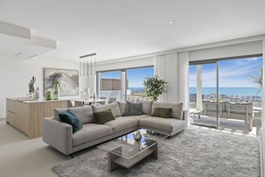 A modern living room with a large sectional sofa, a glass coffee table, and a view of the ocean through large windows.