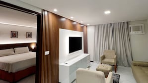 A modern hotel room with a bed, a TV mounted on a wooden panel, a sofa, and a chair. - Ambassador (João Pessoa)