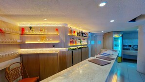 A bar area with shelves of bottles and glasses, a counter with menus, and a refrigerator in the background. - Ambassador (João Pessoa)