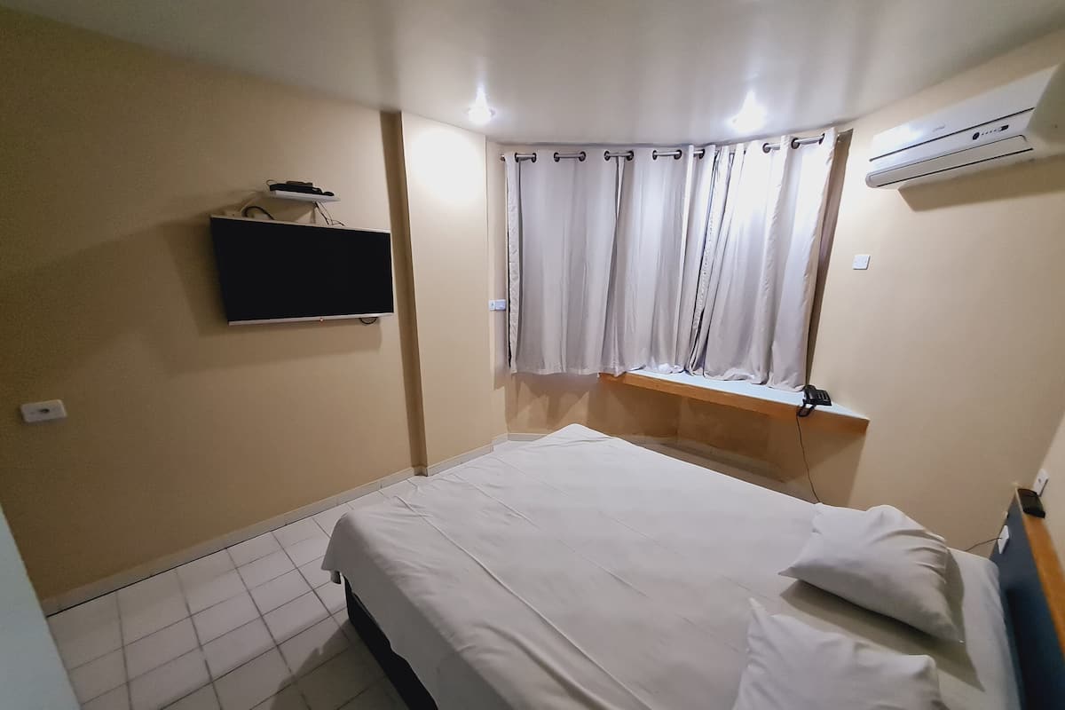 Une chambre à coucher comprenant un lit, un téléviseur fixé au mur, une fenêtre avec des rideaux et un appareil de climatisation.