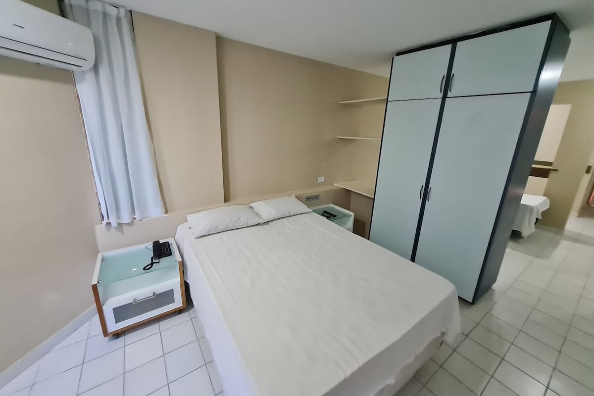 Une chambre d’hôtel équipée d’un lit, d’une armoire, d’une table de chevet, d’un climatiseur et d’un rideau.