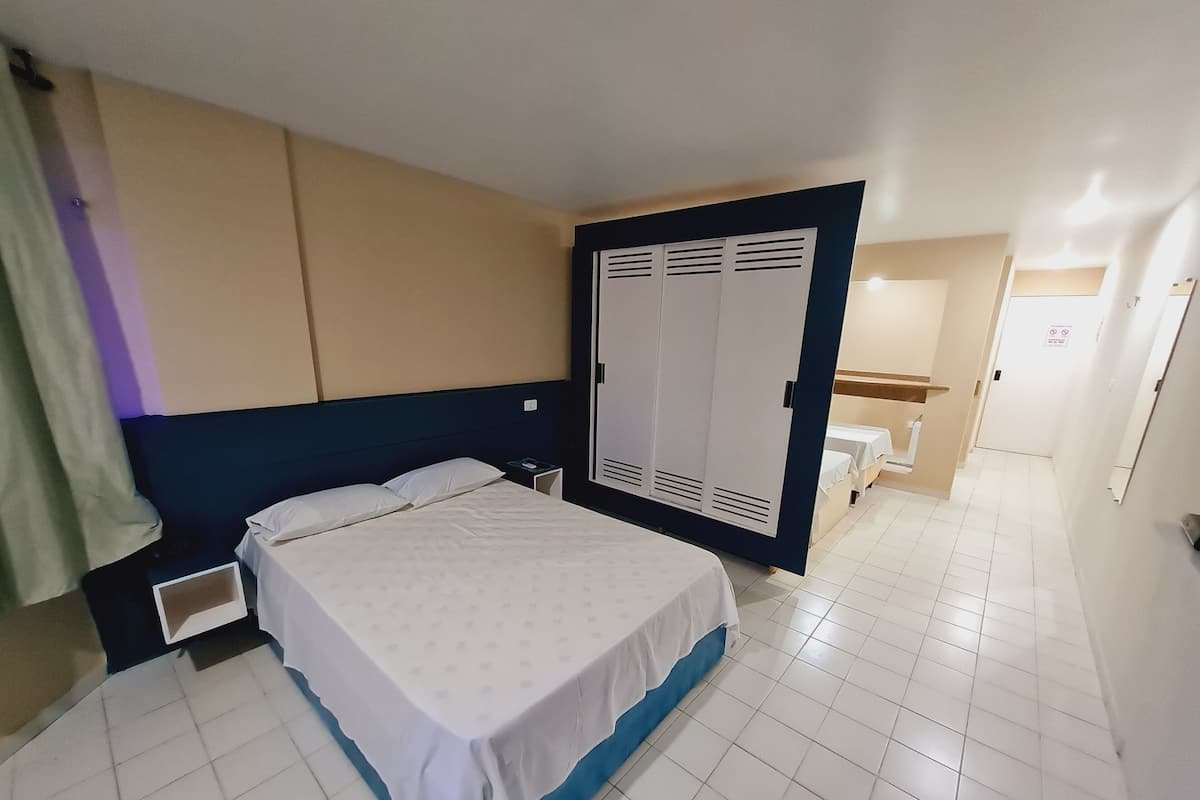 Une chambre d’hôtel avec un lit, une armoire, une table de chevet et une salle de bain visible à travers une porte ouverte.