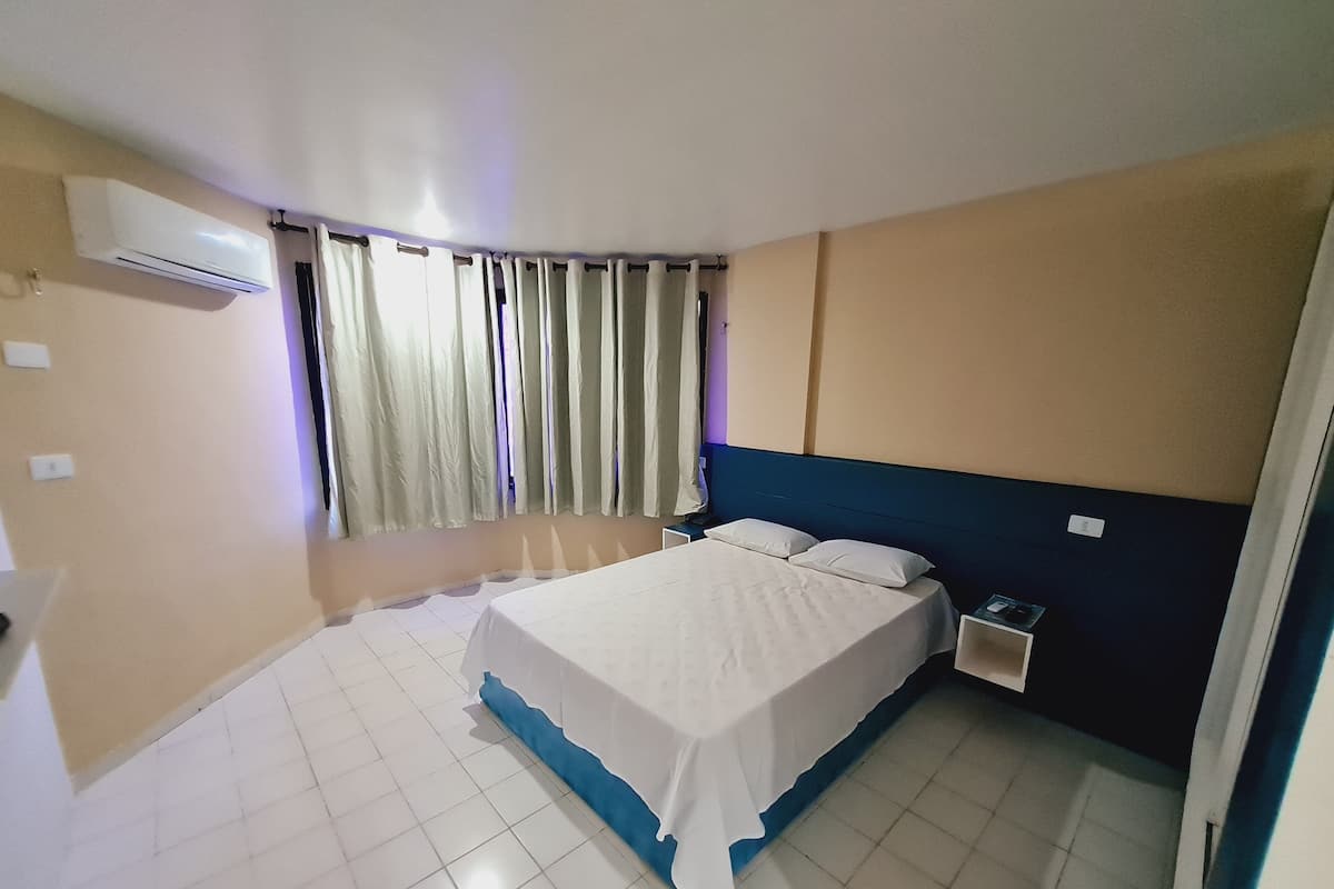 Une chambre à coucher comprenant un lit, une table de chevet, un appareil de climatisation et des rideaux.