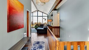 Een modern interieur met een houten trap, een groot abstract schilderij en uitzicht op een zithoek met een bank en salontafel.