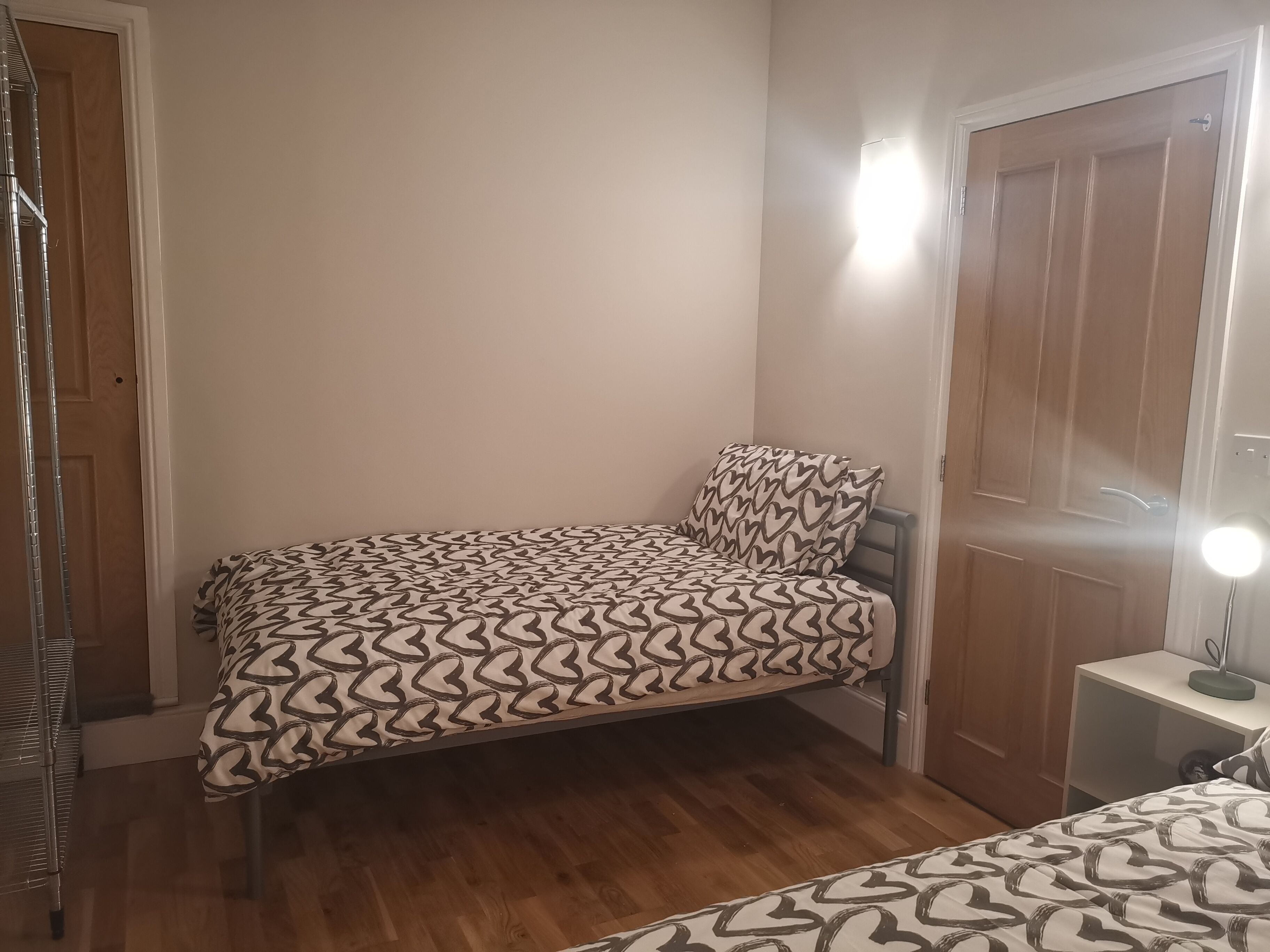 A small bedroom with a bed, a nightstand, a door, and a mirror.
