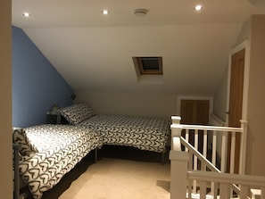 Un dormitorio con techo inclinado, una cama con ropa de cama estampada, un ventanal pequeño y una barandilla blanca.