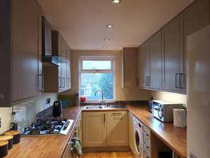 Una cocina moderna con armarios grises, estufa integrada, lavadora y ventana con vistas al exterior.