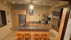 Una cocina con una isla central, cuatro taburetes de bar, un refrigerador y un ventilador de techo.