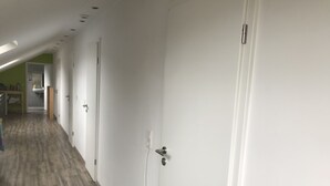A corridor with white doors, a wooden floor, and a visible electrical outlet on the wall. - Single room (Homberg (Efze))