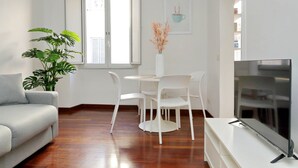 A modern living room with a sofa, a dining table with chairs, a TV on a stand, and a potted plant. - Domus Lou Luxury Apartment in Trastevere Rome (Roma)