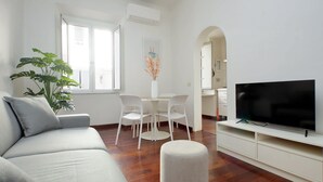 A modern living room with a sofa, a TV, a dining table with chairs, and a potted plant. - Domus Lou Luxury Apartment in Trastevere Rome (Roma)