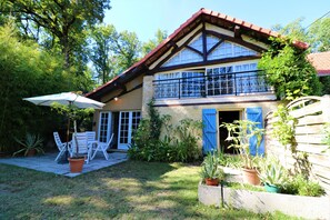 A two-story house with a balcony, a patio with chairs and an umbrella, and various potted plants. - Wellness villa in the countryside with saltwater pool and sauna (Simorre, Brandelin)