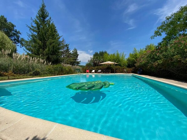 A clear blue pool with a green inflatable toy, surrounded by trees and a covered seating area. - Wellness villa in the countryside with saltwater pool and sauna (Simorre, Brandelin)