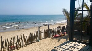 Une vue sur la plage depuis une terrasse en bois, avec une clôture en bois et un kayak rouge.
