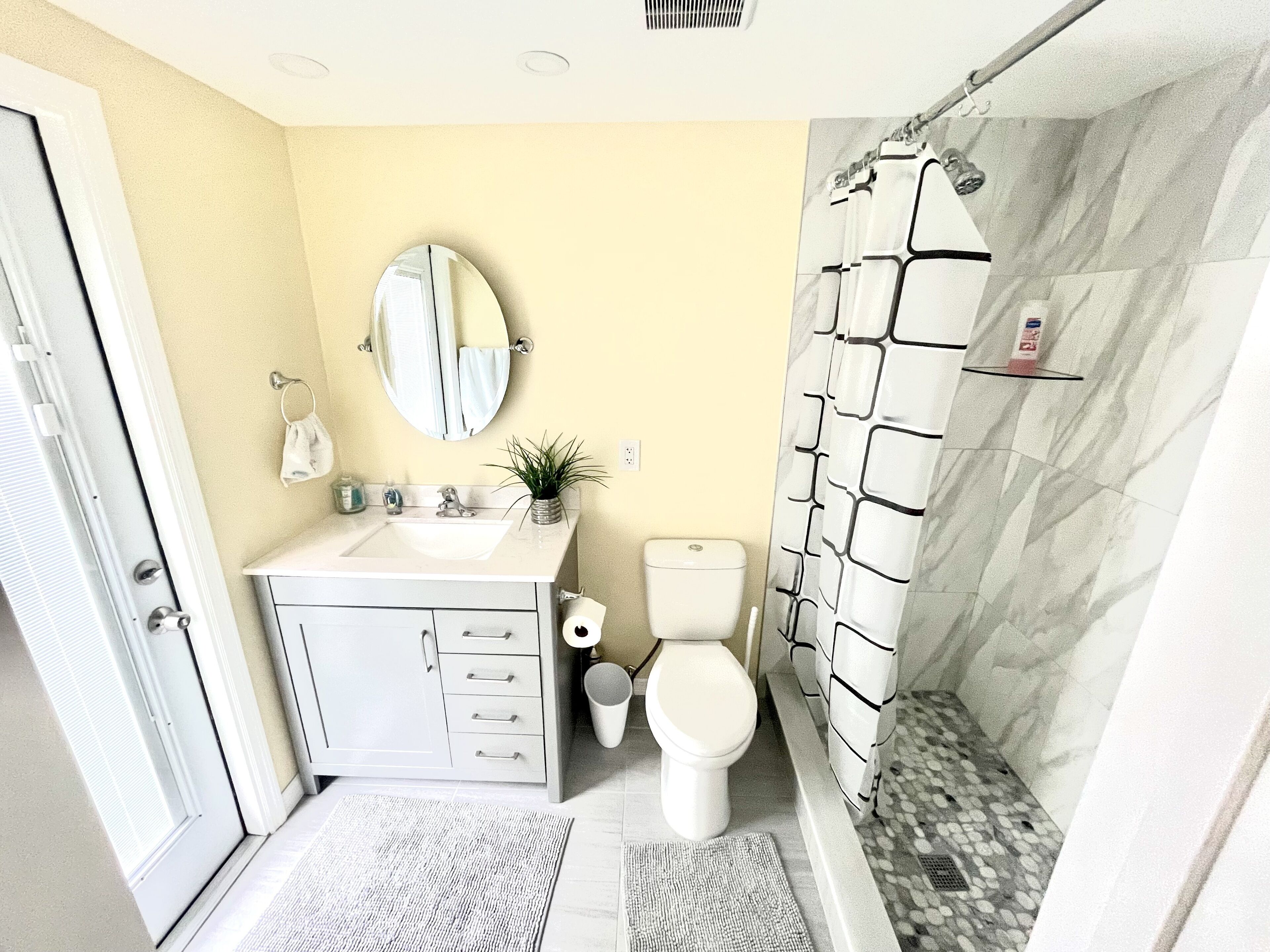A bathroom with a white sink, a round mirror, a toilet, and a shower with a marble wall.