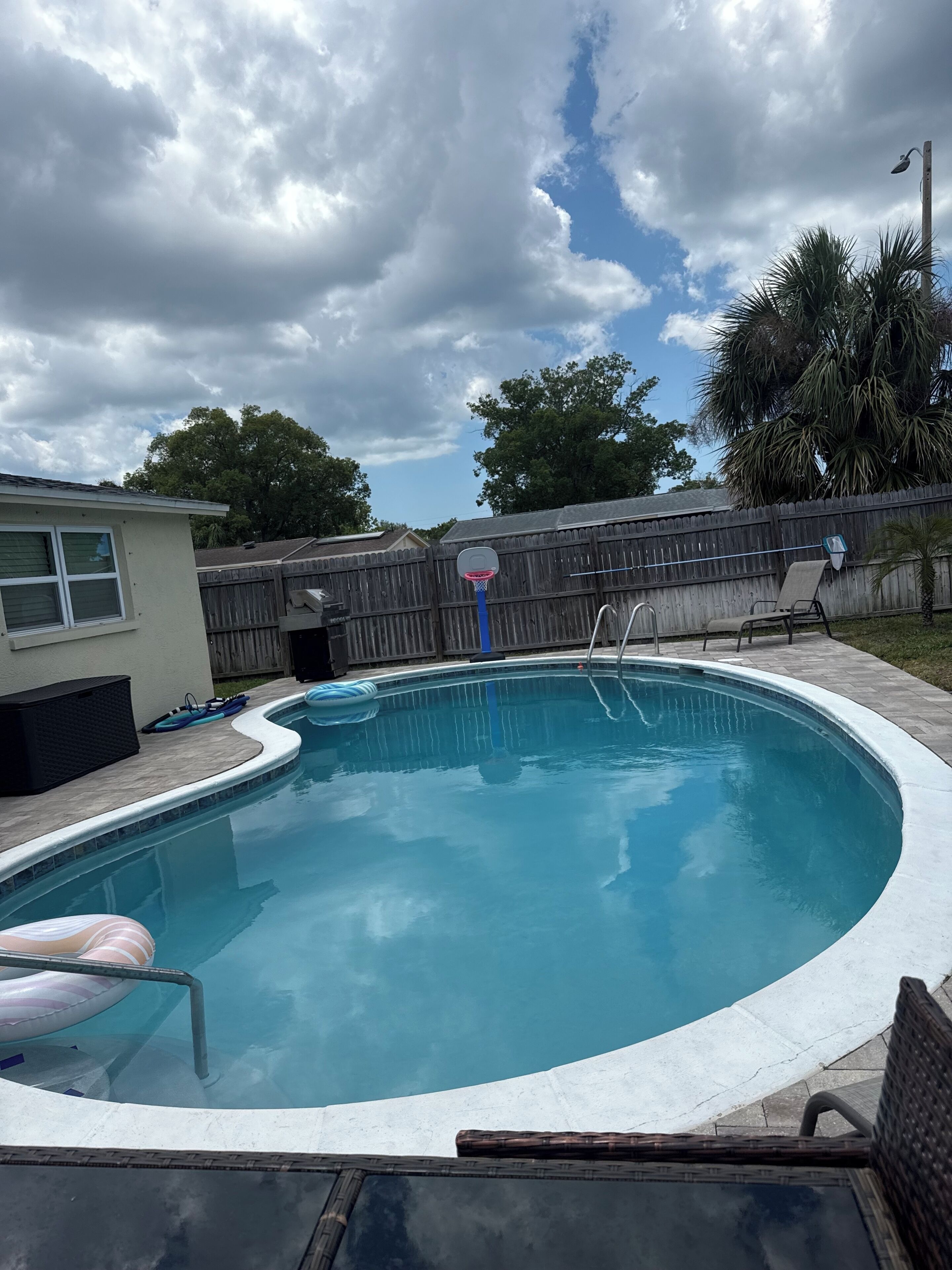Un jardin avec une piscine, un panier de basketball et une clôture en bois.