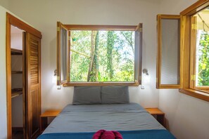 Ein Schlafzimmer mit einem Bett, einem Fenster mit Blick auf Bäume, einem Holzschrank und einem Nachttisch.