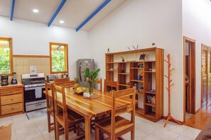 Een keuken met een eettafel, stoelen, een koelkast en een boekenkast.