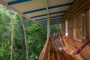 A wooden interior with a hammock, a wooden floor, and a view of a dense forest.
