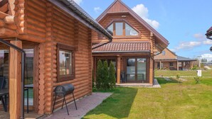 Une cabane en rondins avec une véranda, un barbecue et une cour gazonnée.