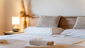 Ein ordentlich bezogenes Bett mit weißen Leinen und zwei Kissen, eine Nachttischlampe und eine Vase mit getrocknetem Pampasgras.