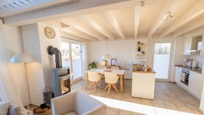 A spacious living area with a sofa, a dining table with chairs, a kitchen with a stove, and a fireplace. - Newly built vacation home with many highlights (sauna, fireplace and first lake location) (Nordhorn)