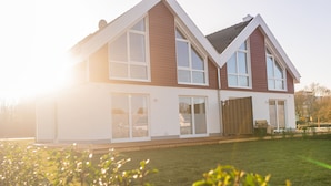 A modern two-story house with large windows and a well-maintained lawn. - Newly built vacation home with many highlights (sauna, fireplace and first lake location) (Nordhorn)