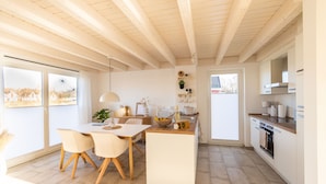 A modern kitchen with a central island, wooden beams, and large windows. - Newly built vacation home with many highlights (sauna, fireplace and first lake location) (Nordhorn)