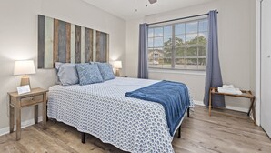 Une chambre à coucher comprenant un lit, des tables de chevet, un ventilateur de plafond, une fenêtre avec des rideaux et un mur orné de panneaux de bois.
