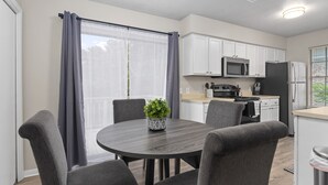 Une cuisine moderne avec des meubles blancs, un four à micro-ondes et un réfrigérateur. On y trouve également un coin repas avec une table ronde et quatre chaises.