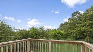 Une terrasse en bois dotée d’une balustrade, qui donne sur une zone herbeuse parsemée d’arbres.