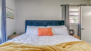 Une chambre à coucher avec un lit, une table de chevet, une fenêtre avec des rideaux et une porte.