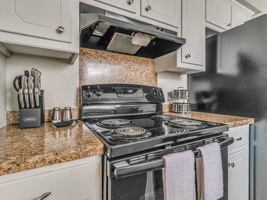 A kitchen with a black stove, granite countertop, and white cabinets.