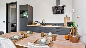 A modern kitchen with dark cabinetry, a built-in oven, and a gas stove. There is a dining table set with plates, cups, and a vase with flowers. - 3 bedroom beautiful home in Den Oever (Den Oever)