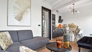 A modern living room with a grey sofa, a round coffee table, and a black ottoman. There is a dining area with a table and chairs visible in the background. - 3 bedroom beautiful home in Den Oever (Den Oever)