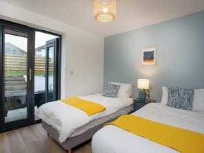 Et moderne soveværelse med to senge, en skydedør til en balkon og et lille natbord med en lampe.