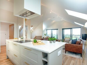 A modern kitchen with a central island, a dining area with a sofa, and large windows offering a view. - 4 bedroom accommodation in Tintagel (Tintagel)