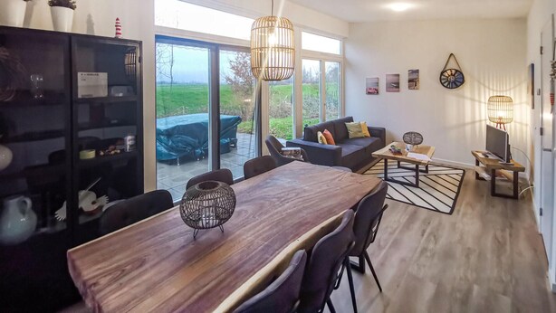 Una sala de estar moderna con una mesa de comedor de madera, sillas negras, un sofá y un amplio ventanal con vistas al exterior.
