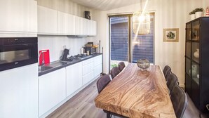 Cocina moderna con armarios blancos, un microondas negro y una tabla de cortar roja. Hay una mesa de comedor de madera con sillas y una araña.