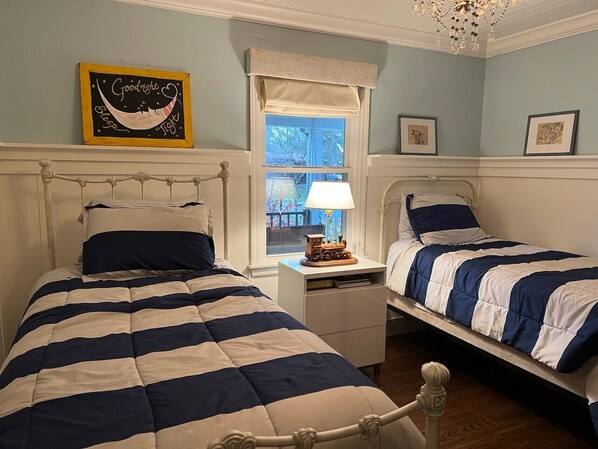 Un dormitorio con dos camas, una mesita de noche con lámpara, una ventana con vistas y una pared decorada con cuadros.