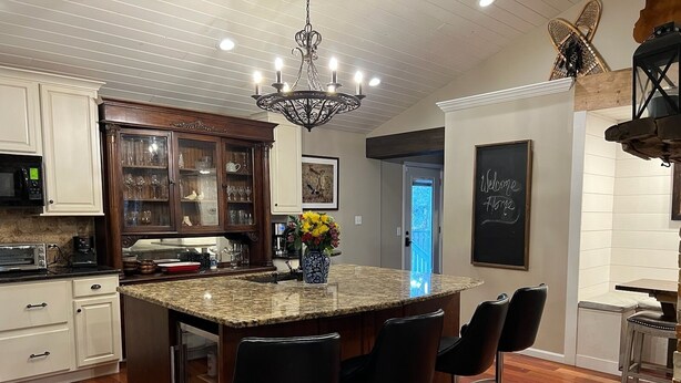 A modern kitchen with a central island, bar stools, wooden cabinets, and a chandelier.