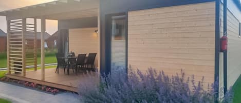 A modern house with a covered patio, a dining area, and a garden with purple flowers.